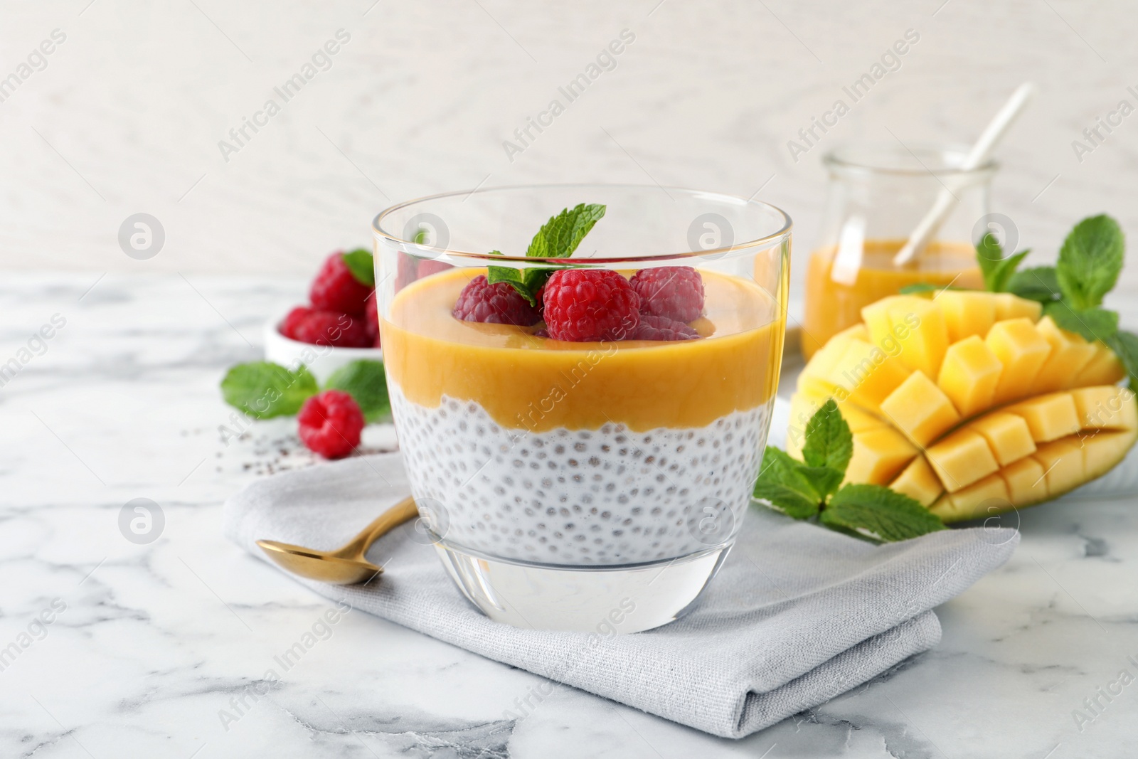 Photo of Delicious chia pudding with mango sauce and raspberries on white marble table