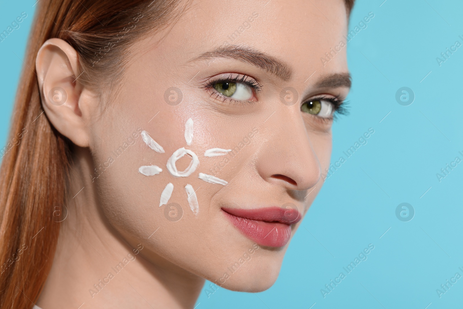 Photo of Beautiful young woman with sun protection cream on her face against light blue background, closeup. Space for text