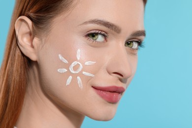 Beautiful young woman with sun protection cream on her face against light blue background, closeup. Space for text