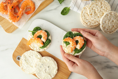 Photo of Woman holding crunchy rice cake with shrimps and basil at white marble table, top view