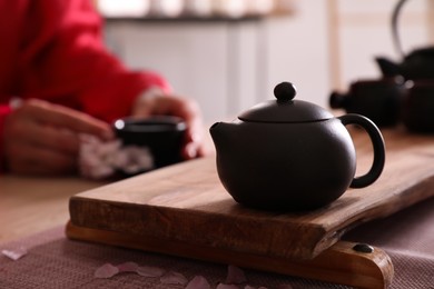 Photo of Traditional tea ceremony, focus on teapot. Guest holding cup at table, closeup