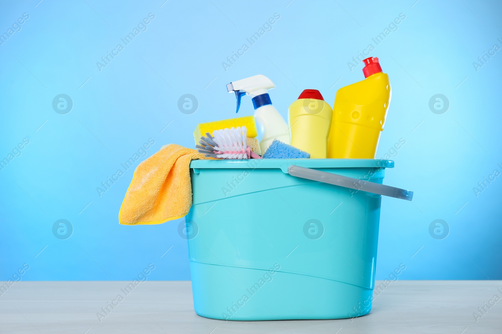 Photo of Bucket with different cleaning products and supplies on light table