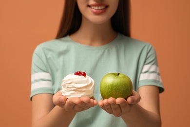 Photo of Woman choosing between apple and cake on orange background, closeup