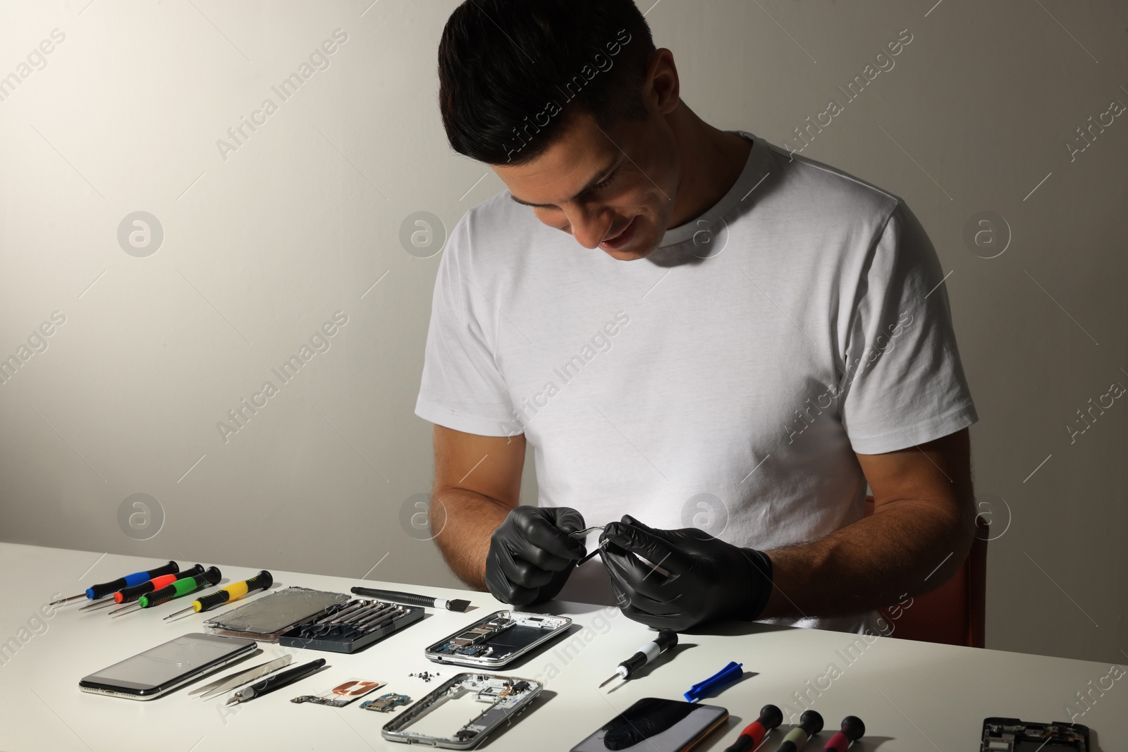 Photo of Technician repairing broken smartphone at table indoors
