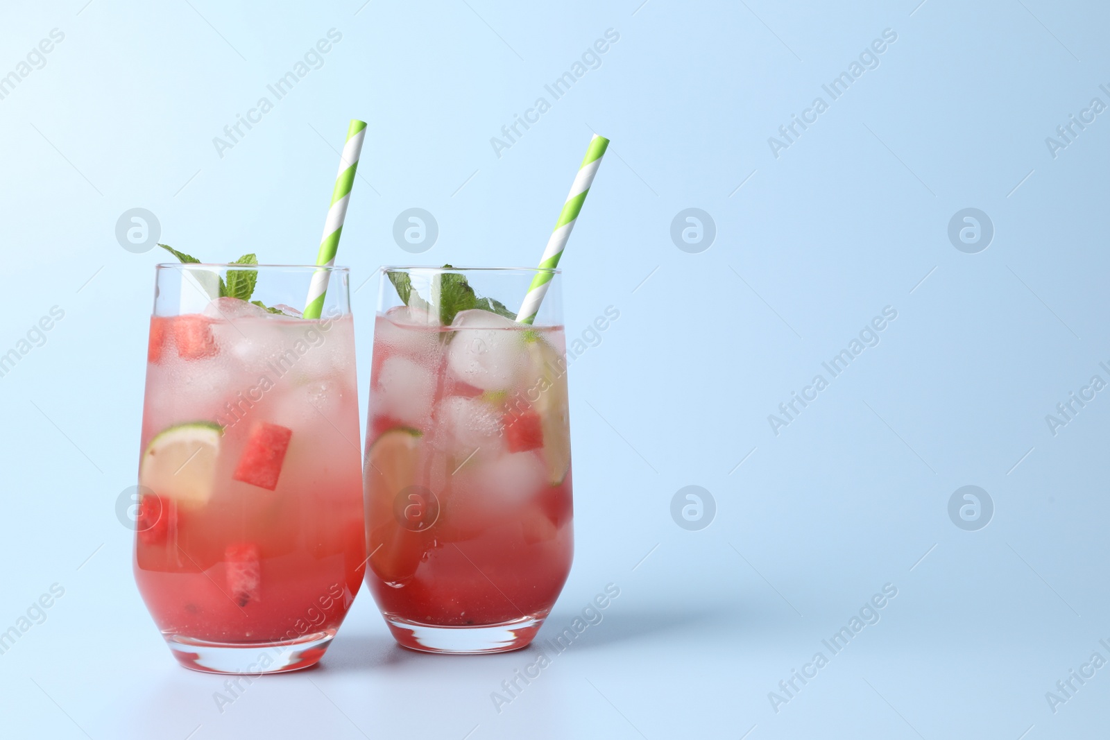 Photo of Tasty summer watermelon drink with lime in glasses on pale light blue background. Space for text