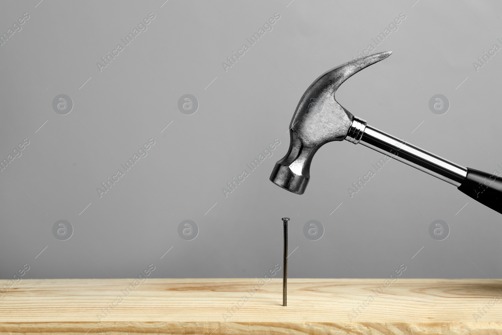 Photo of Hammering nail into wooden surface against grey  background, space for text