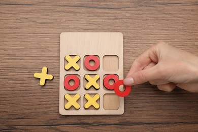 Photo of Woman playing tic tac toe game at wooden table, top view