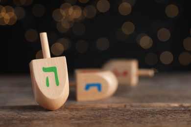 Photo of Hanukkah traditional dreidel with letter He on wooden table against blurred lights, space for text
