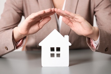 Photo of Female agent covering house model at table, closeup. Home insurance