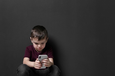 Sad little boy with mobile phone on black background, space for text