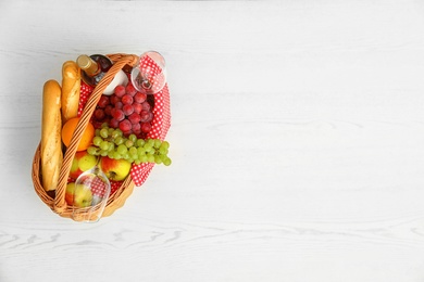 Picnic basket with products and wine on white wooden table, top view. Space for text