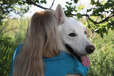 Photo of Young woman hugging her white Swiss Shepherd dog in park, back view