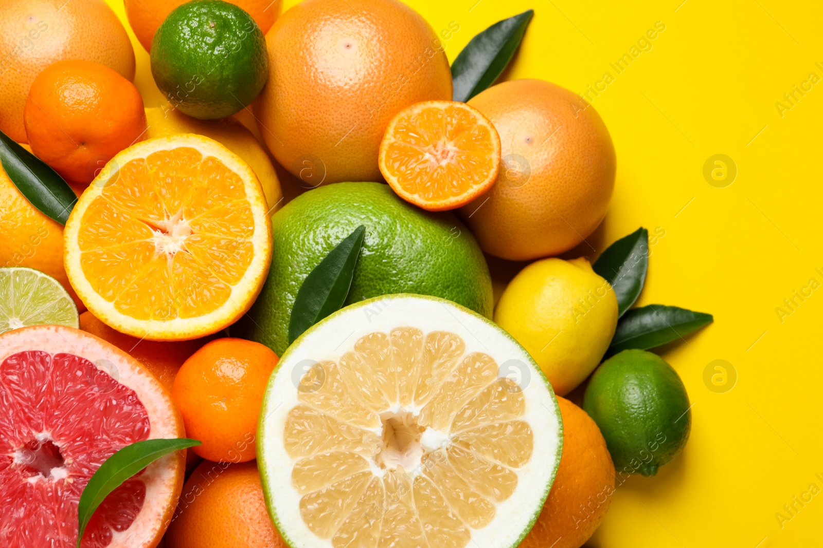 Photo of Different ripe citrus fruits with green leaves on yellow background, flat lay