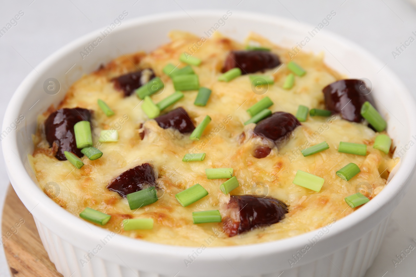 Photo of Tasty sausage casserole with green onions in baking dish on table, closeup