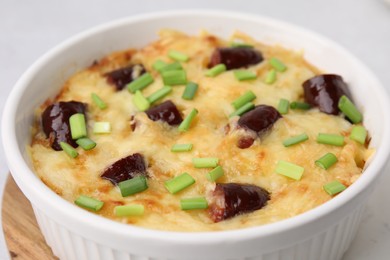 Photo of Tasty sausage casserole with green onions in baking dish on table, closeup