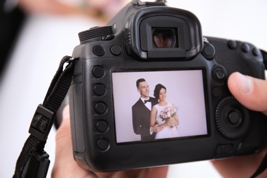 Professional photographer holding camera with lovely wedding couple on display, closeup