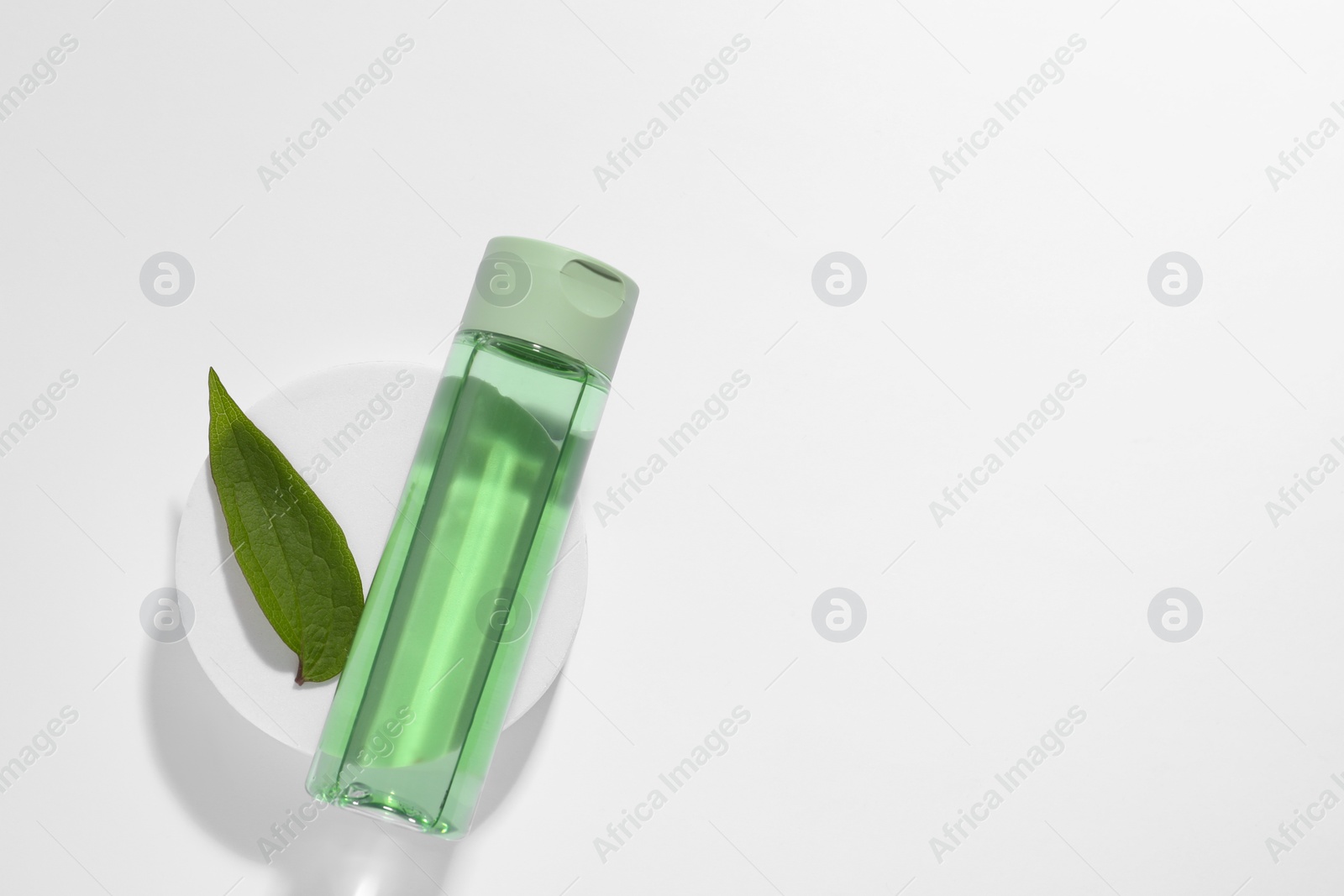 Photo of Bottle of cosmetic product, green leaf and podium on white background, top view. Space for text