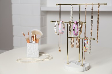 Holder with set of luxurious jewelry and makeup brushes on white table