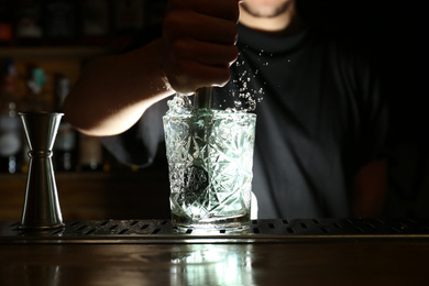 Photo of Bartender preparing fresh alcoholic cocktail at bar counter, focus on glass