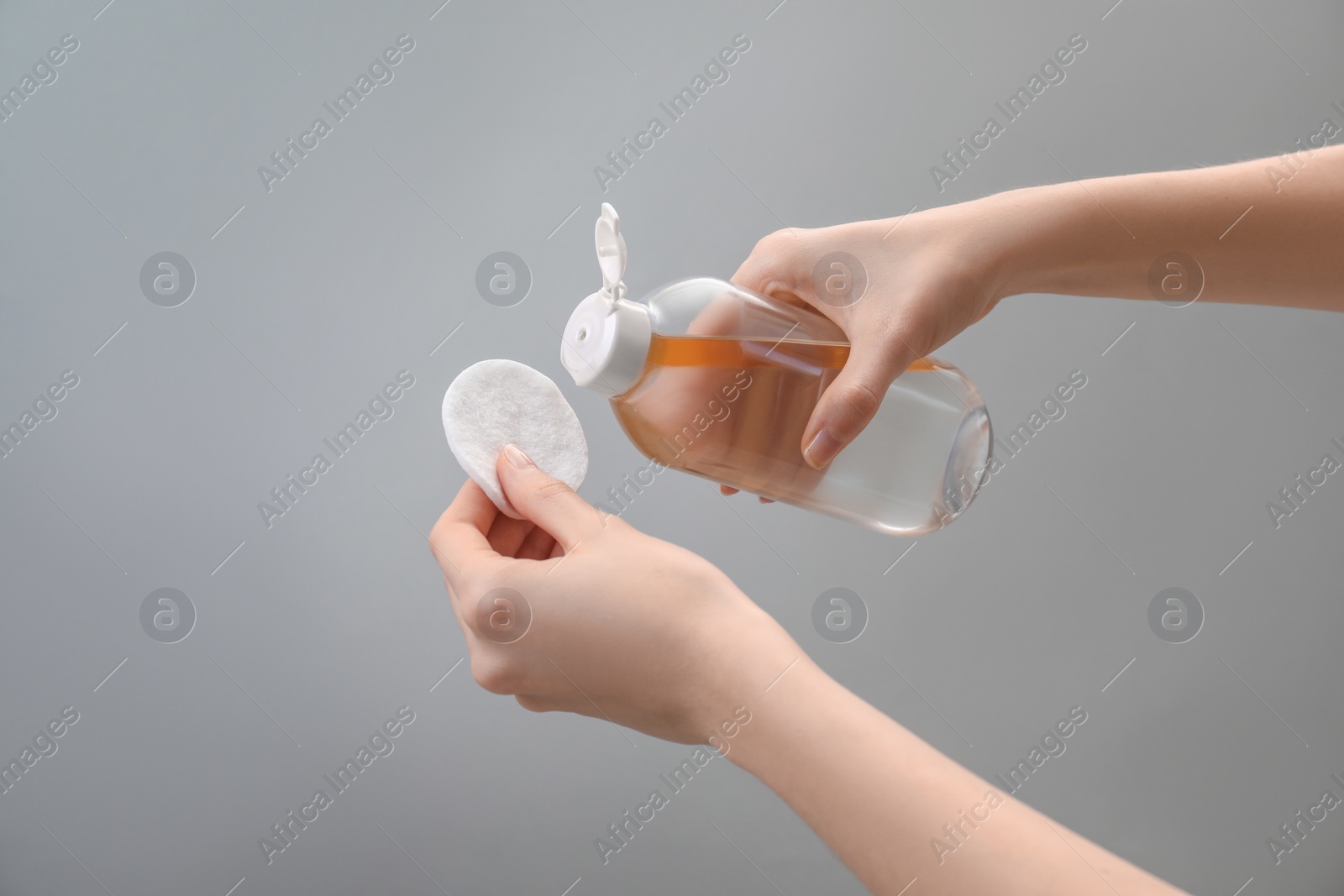 Photo of Woman pouring makeup remover onto cotton pad on light grey background, closeup