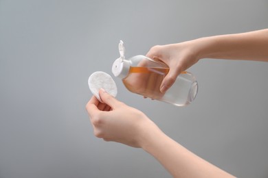 Woman pouring makeup remover onto cotton pad on light grey background, closeup