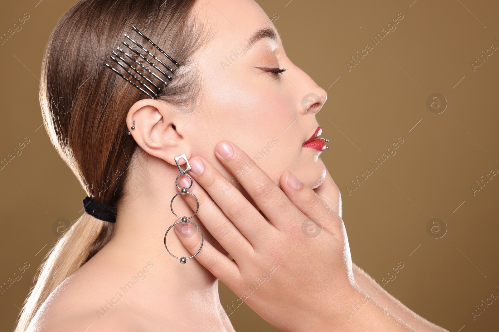 Photo of Piercing master touching model's face on light brown background, closeup
