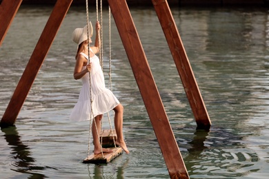 Young woman on swing over water on sunny day