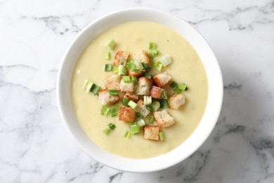 Tasty potato soup with croutons and green onion in bowl on white marble table, top view