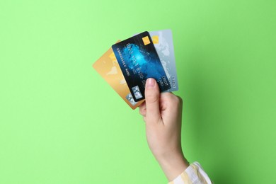 Woman holding credit cards on light green background, closeup