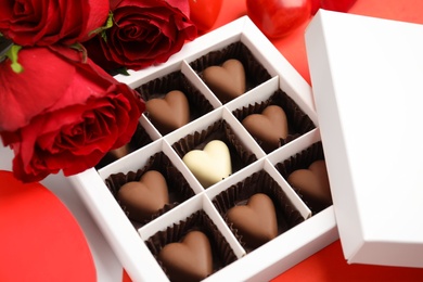 Photo of Tasty heart shaped chocolate candies in box and roses on color background. Valentine's day celebration