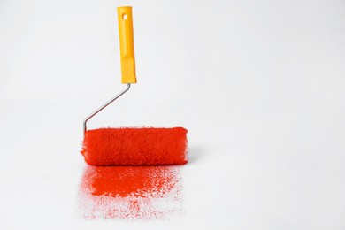 Photo of Roller brush and strokes of orange paint on white background. Space for text