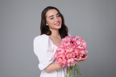 Photo of Beautiful young woman with bouquet of pink peonies on grey background