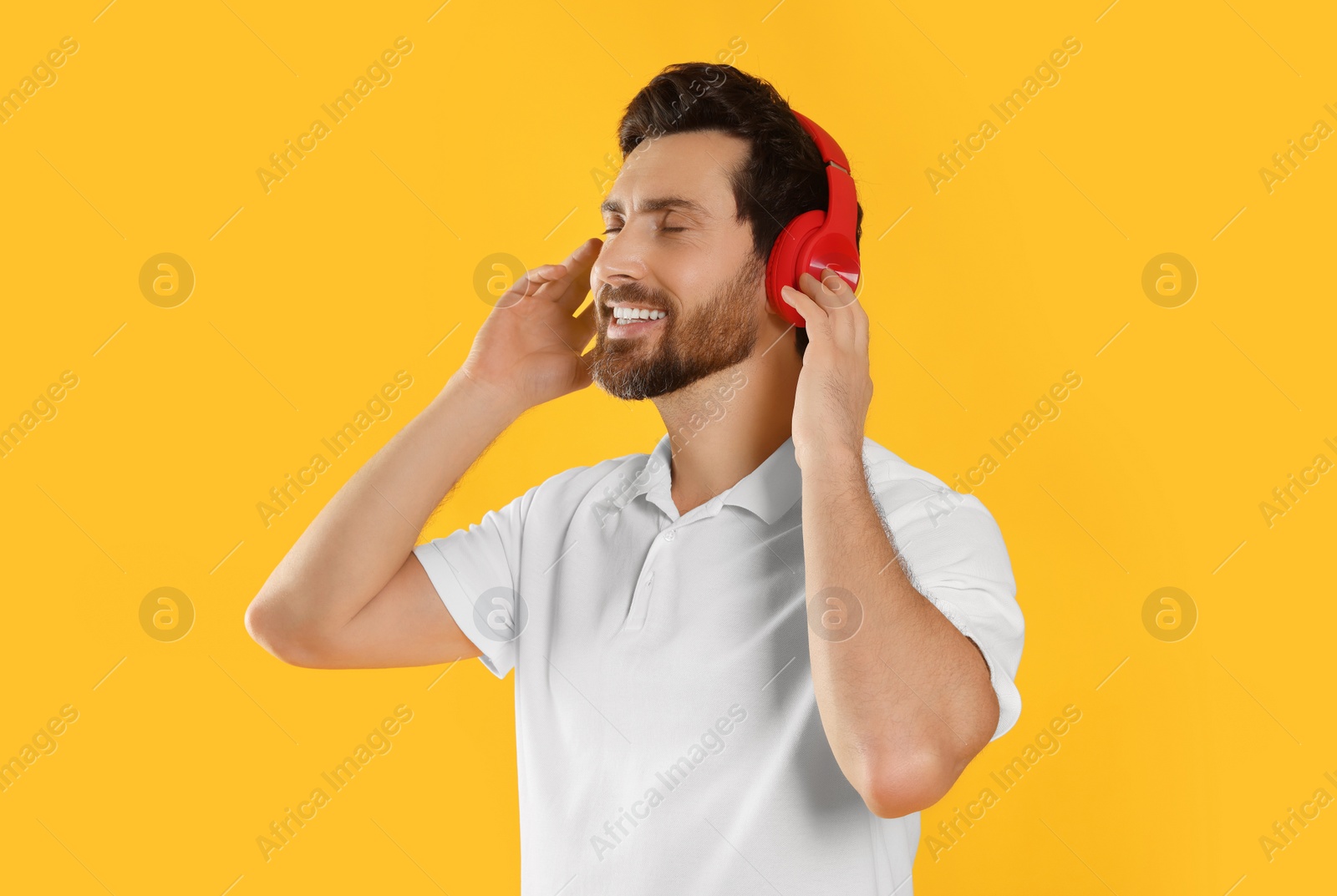 Photo of Happy man listening music with headphones on yellow background
