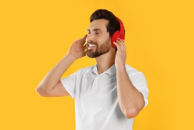 Photo of Happy man listening music with headphones on yellow background