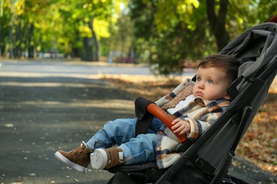 Photo of Cute little child in stroller in autumn park, space for text