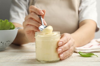 Photo of Woman with jar of delicious mayonnaise at white wooden table, closeup
