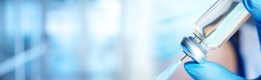 Image of Doctor filling syringe with medication from glass vial on blurred background, closeup. Banner design