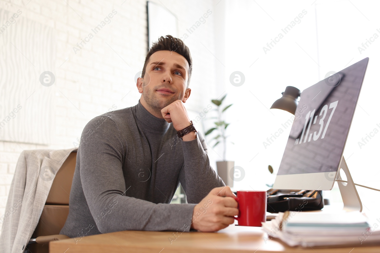 Photo of Young man with cup of drink relaxing at table in office during break