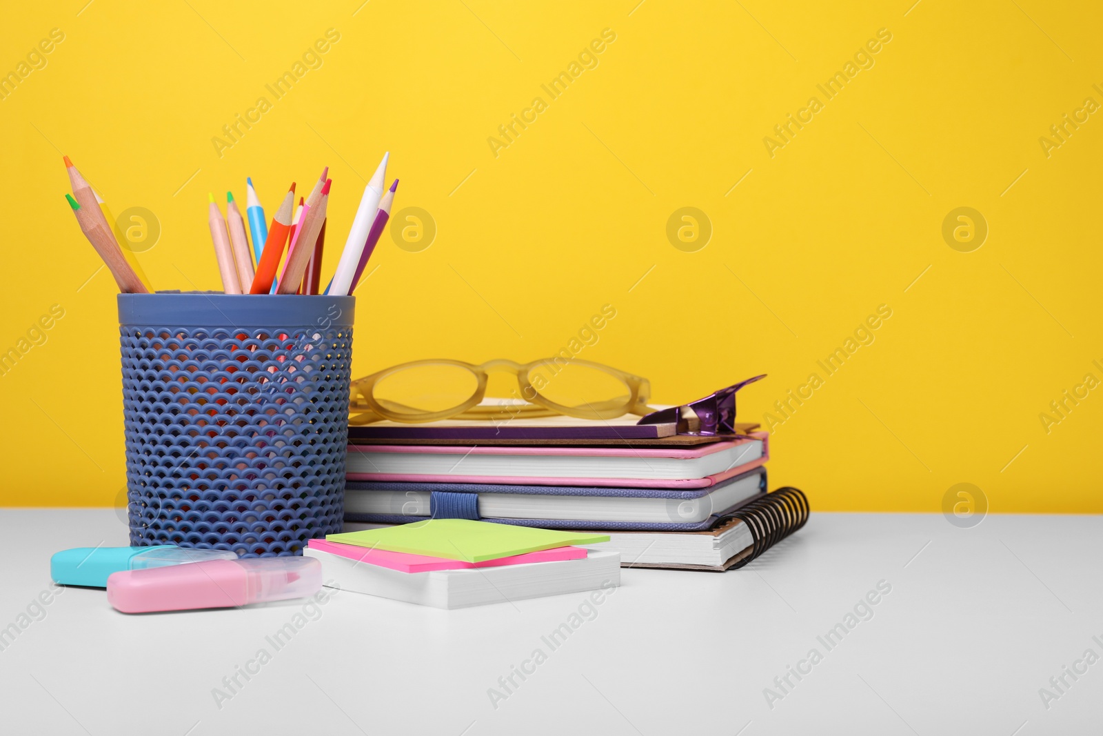 Photo of Different school stationery and glasses on white table against yellow background, space for text. Back to school