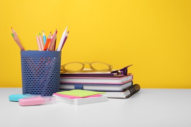 Photo of Different school stationery and glasses on white table against yellow background, space for text. Back to school