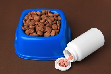 Bowl with dry pet food and bottle of vitamins on brown background, closeup