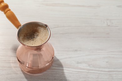 Cezve with hot aromatic Turkish coffee on white wooden table, space for text