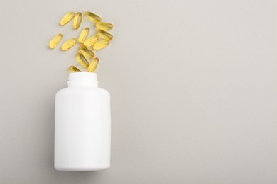 Photo of Bottle and vitamin capsules on light grey background, top view. Space for text