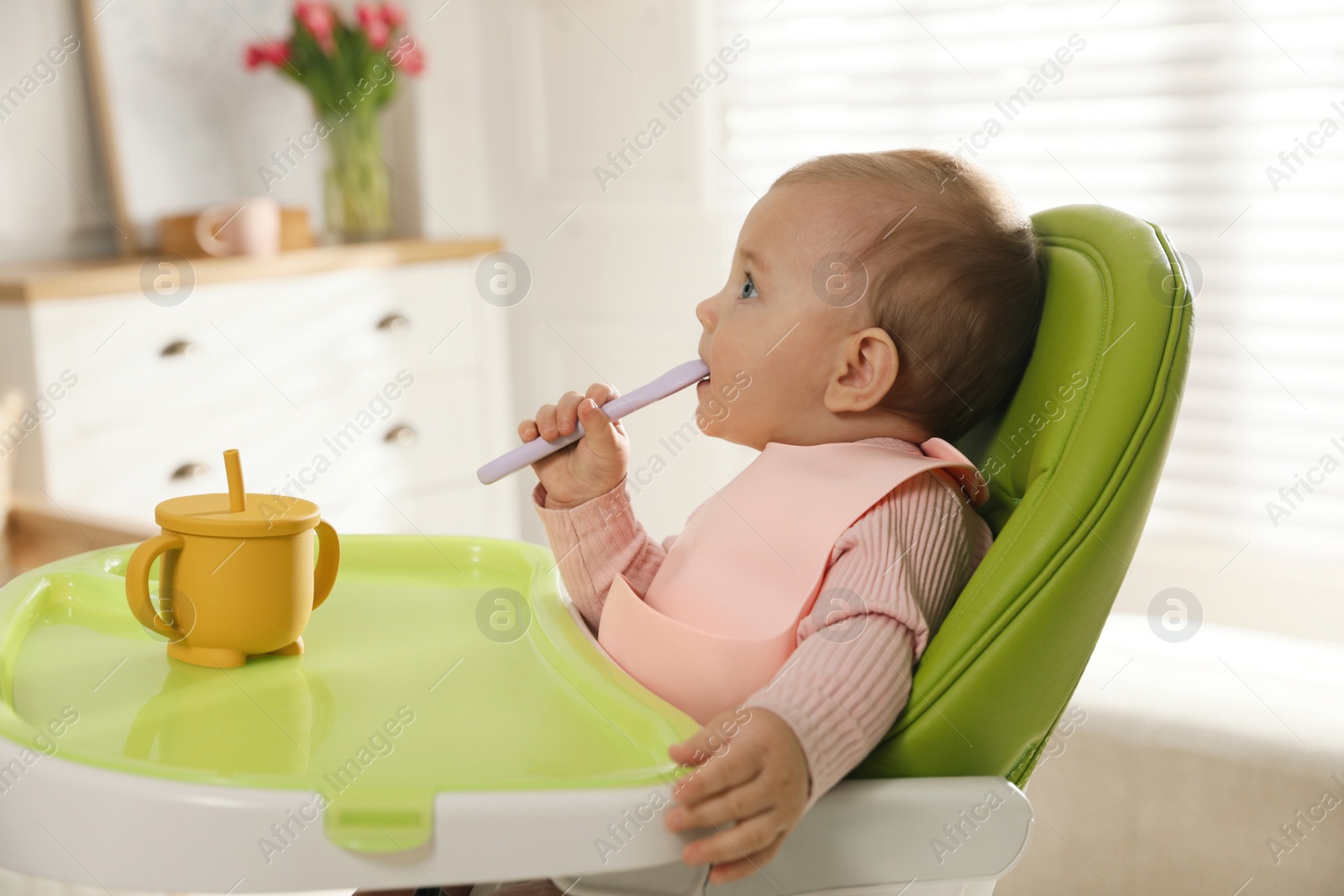 Photo of Cute little baby wearing bib in highchair at home