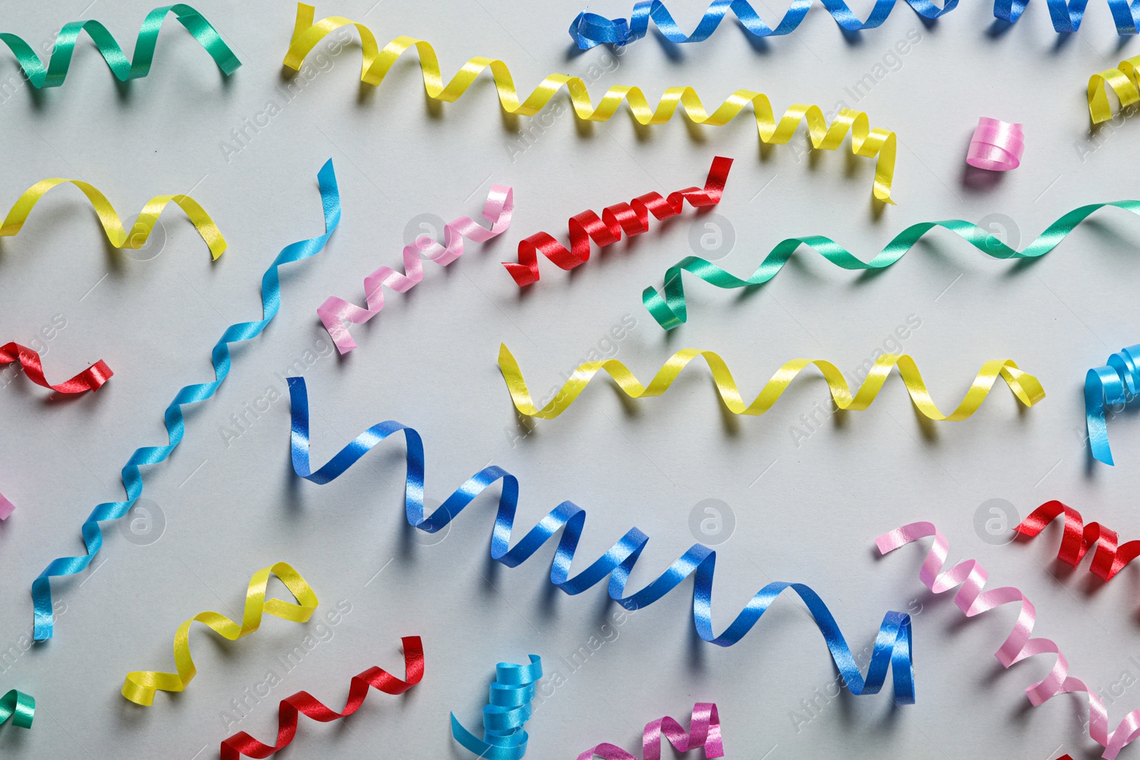 Photo of Colorful serpentine streamers on light background, flat lay