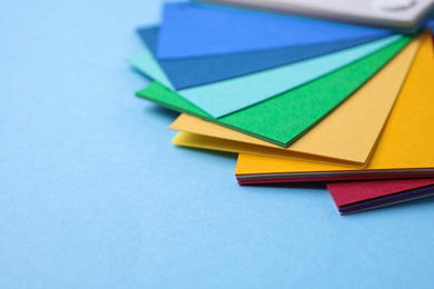 Photo of Multicolored paper sheets on light blue background, space for text. Rainbow palette