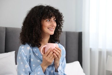 Photo of Beautiful young woman in stylish pyjama with cup of drink at home