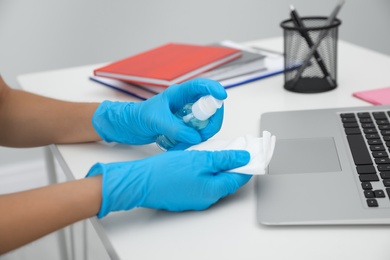 Photo of Woman in latex gloves cleaning her office workplace with antiseptic, closeup
