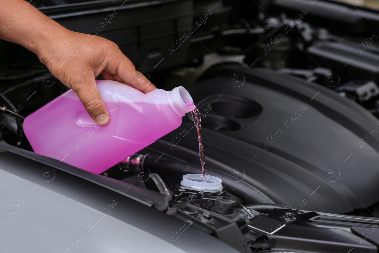 Photo of Man pouring liquid from plastic canister into car washer fluid reservoir, closeup