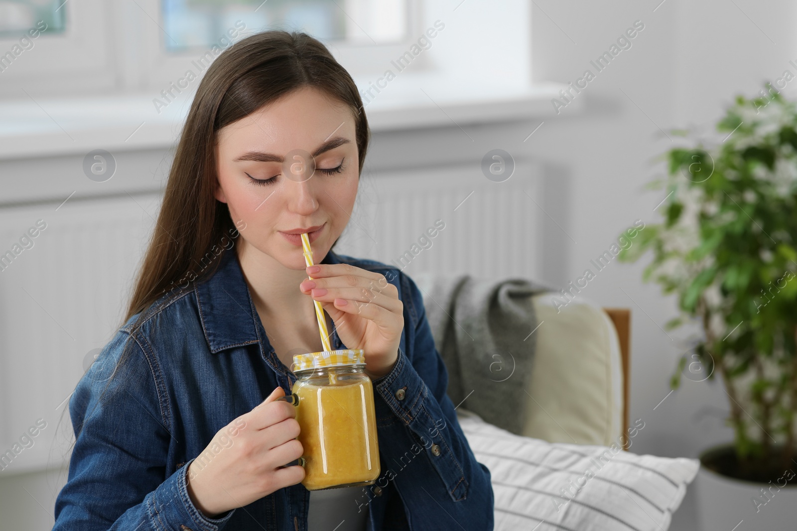 Photo of Beautiful young woman drinking delicious smoothie at home. Space for text